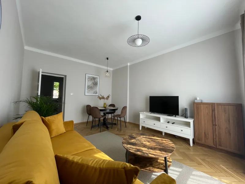 wnętrze apartamentu z widokiem na salon, tv, sofę, stół jadalny oraz stolik kawowy