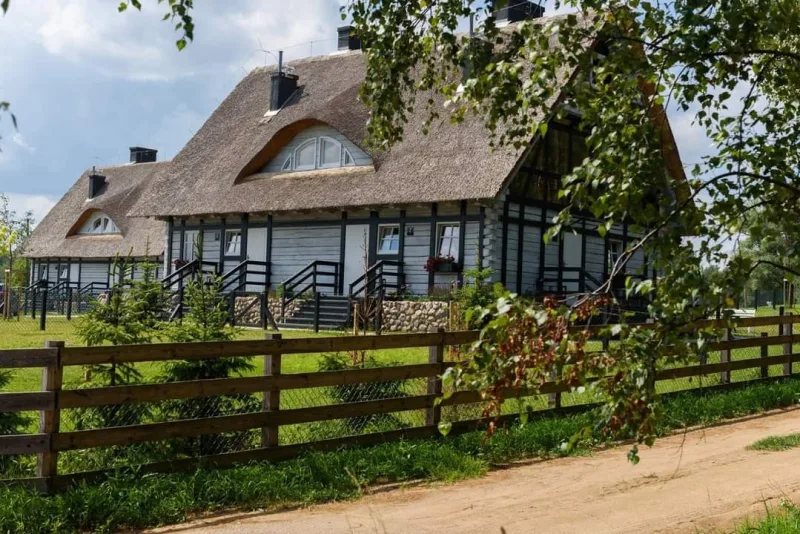 dwa drewniane domy kryte strzechą, wokół ogrodzenie