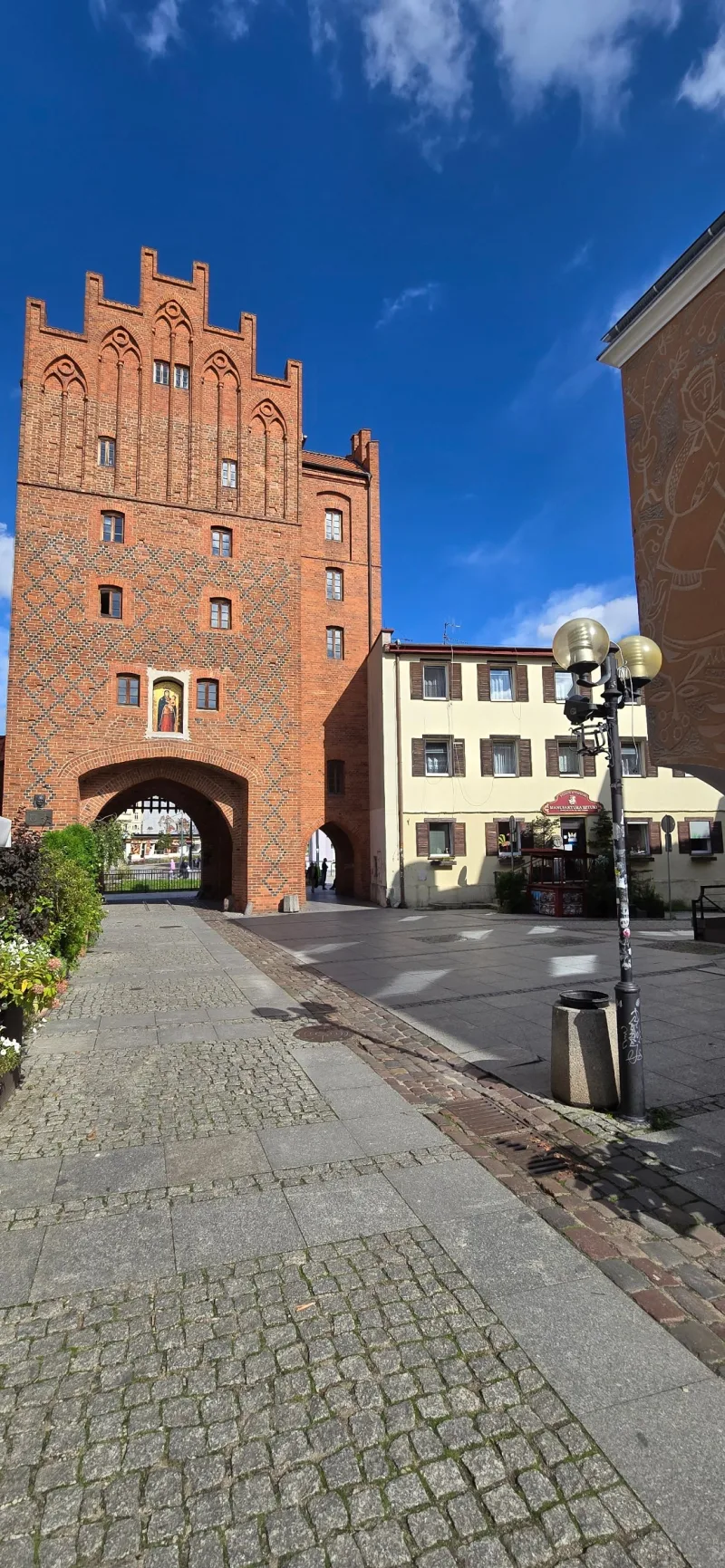 zdjęcie zabytkowej Wysokiej Bramy z czerwonej cegły oraz hostelu od strony Starego Miasta