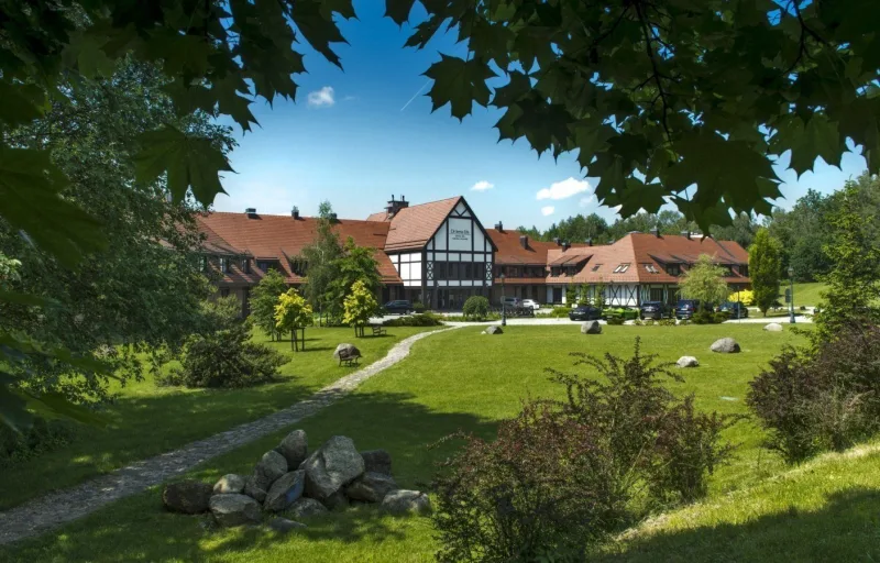 w oddali widok na budynek hotelowy, drzewa, trawa i kamienie