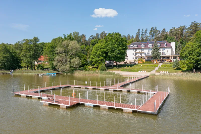 widok na molo na jeziorze oraz na budynek ośrodka w tle pomiędzy drzewami