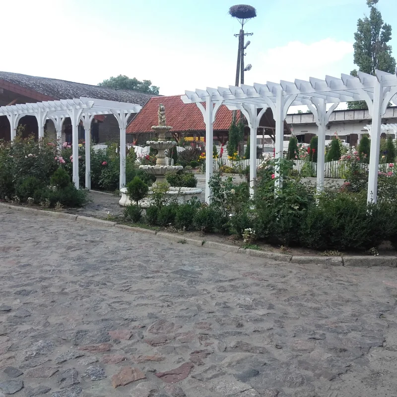 pergola w ogrodzie, fontanna w tle słup z bocianim gniazdem